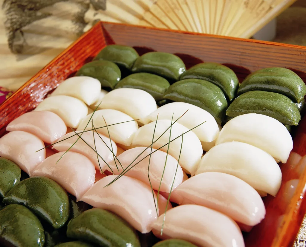 Pink, white, and green songpyeon rice cakes arranged on a wooden tray