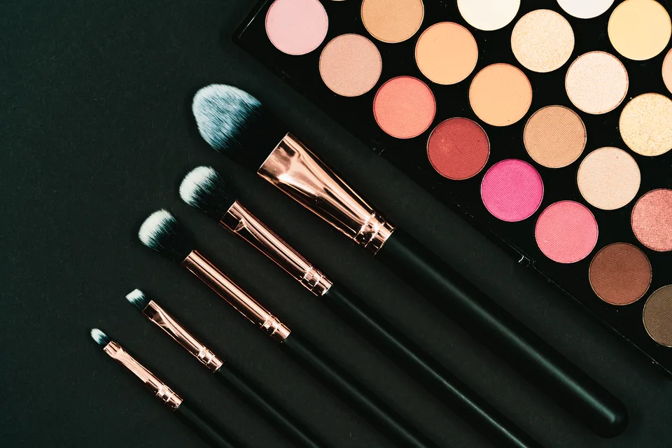 Eyeshadow palette with rose-gold handled makeup brushes on a black background