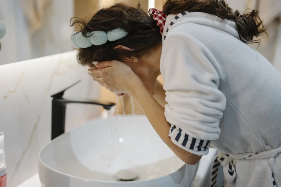 Person washing their face over a bathroom sink