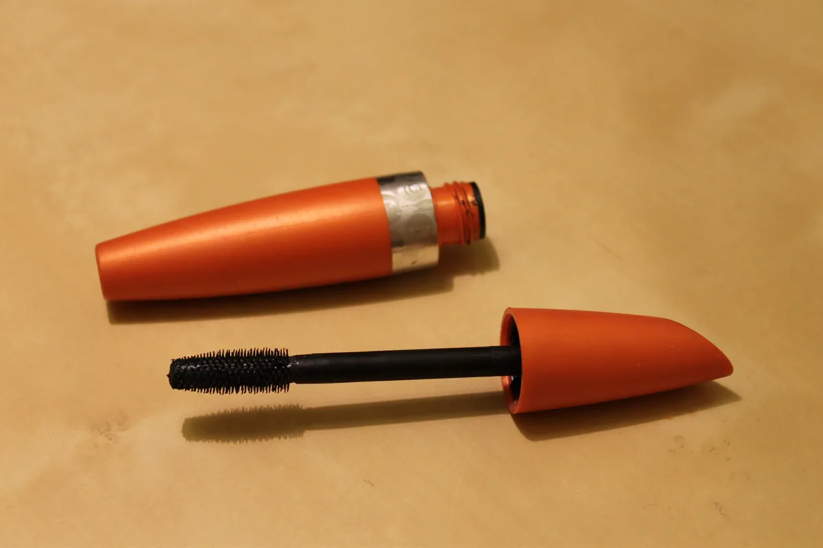 An open mascara tube and wand photographed on a plain background