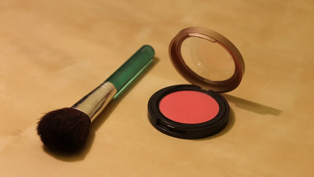 A coral powder blush compact beside a face brush